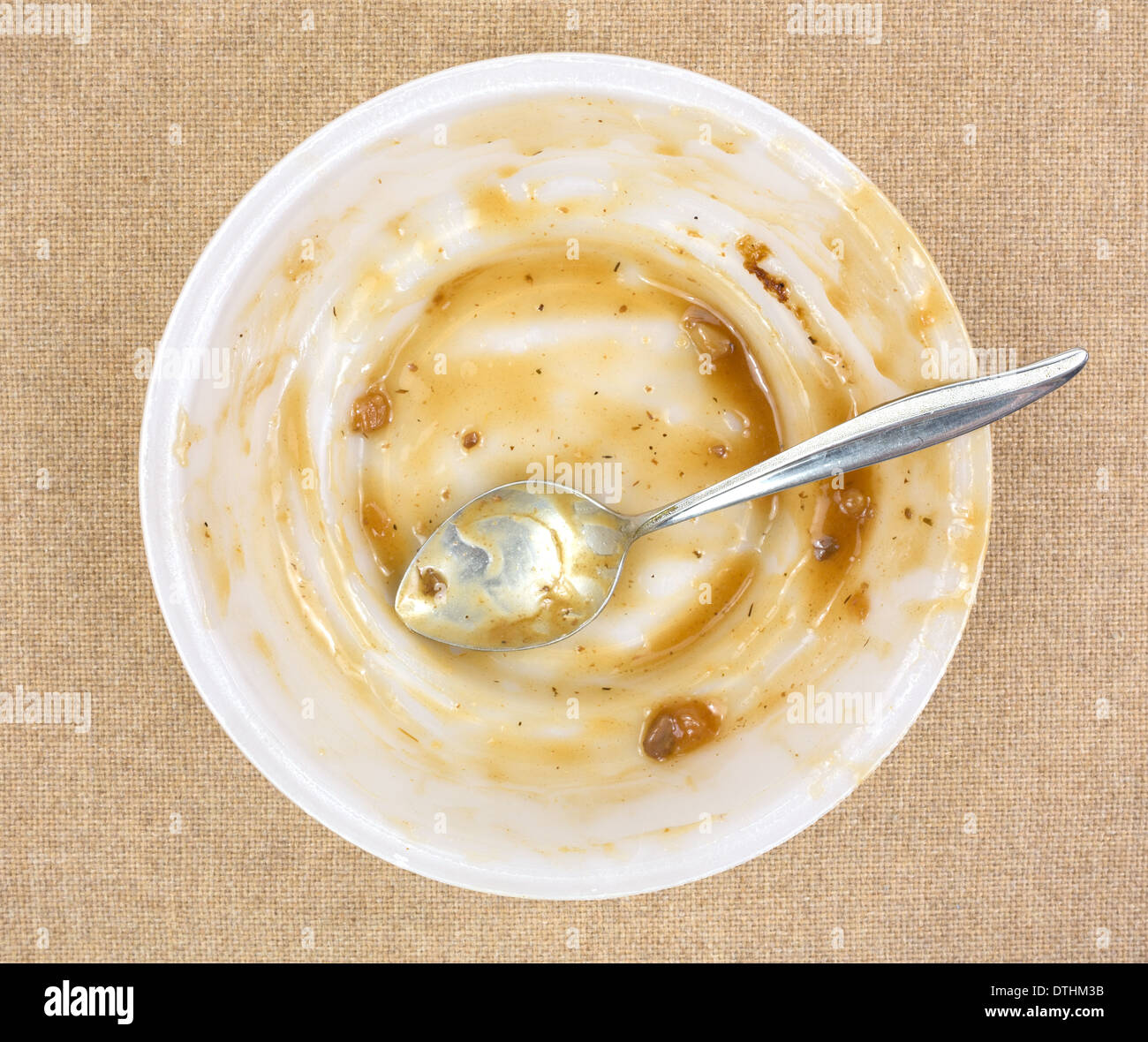 Top view of a finished TV dinner bowl with a spoon on a cloth background. Stock Photo