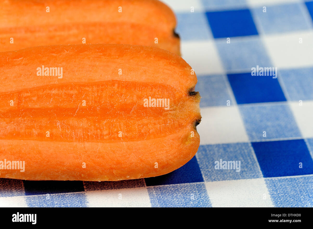 A fresh carrot cut into 2 pieces on a blue gingham background Stock Photo