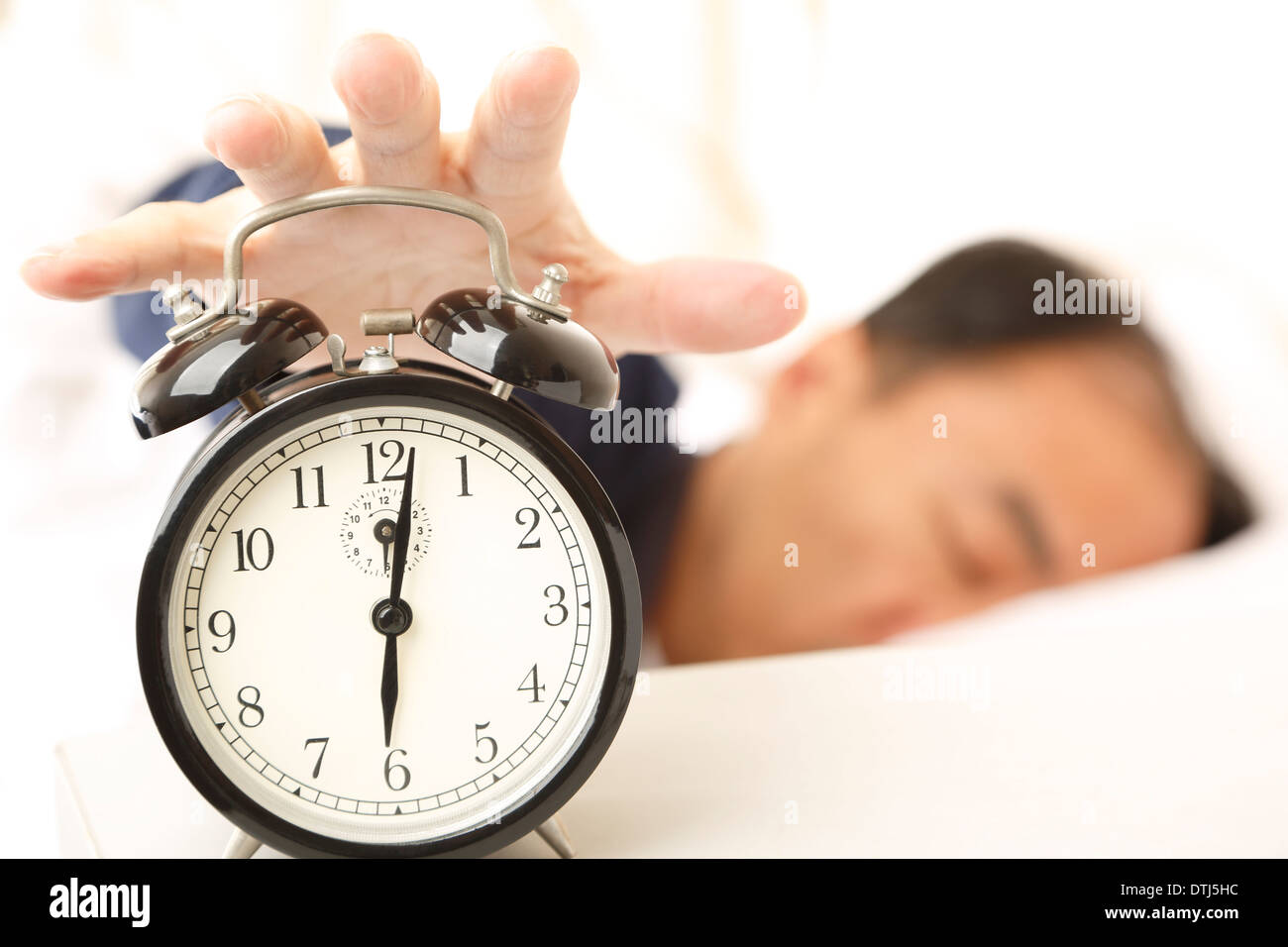 Asian man in sleep, waking up by an alarm clock Stock Photo