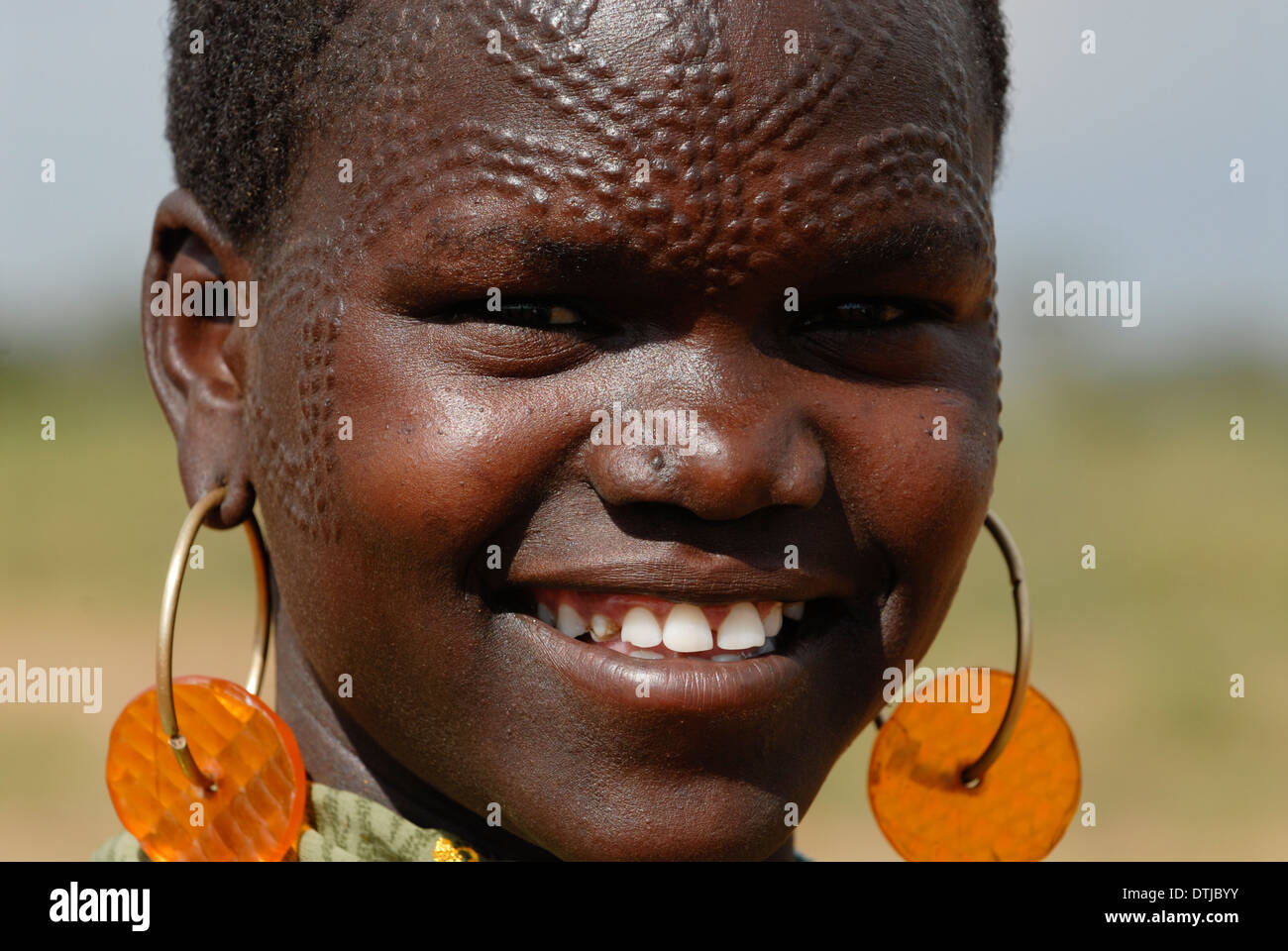 Uganda Karamoja Kotido, Karimojong people, pastoral tribe, woman with face scarification and car blinking light earrings Stock Photo