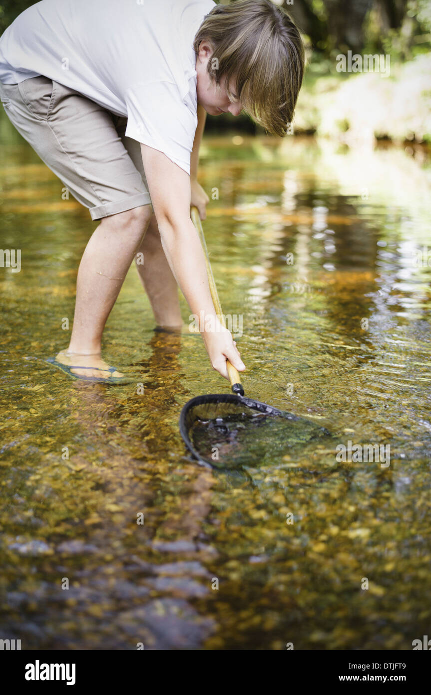 A boy paddling in shallow water leaning over and using a small fishing net  Hampshire England Stock Photo
