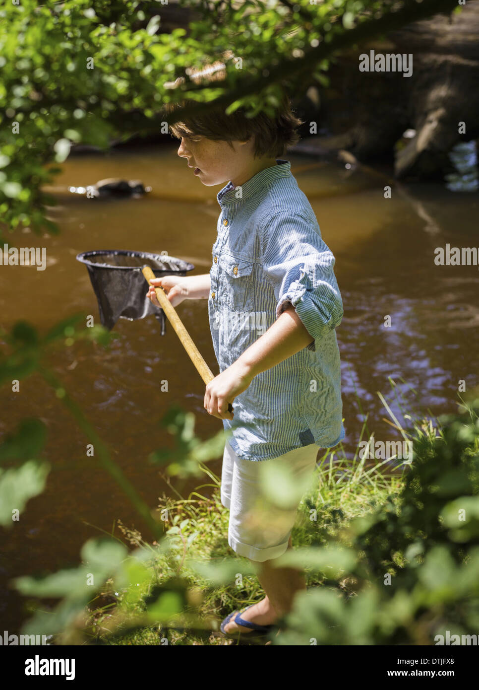 A young boy holding a fishing net by a shallow river Camping in the New Forest Hampshire England Stock Photo