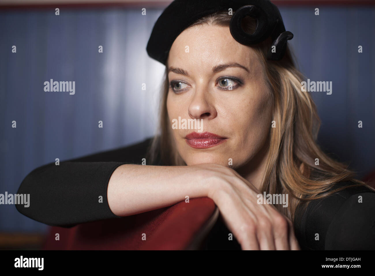 A woman in a theatre wearing an evening hat and black top Resting her chin on her hand looking away in an elegant pose Stock Photo