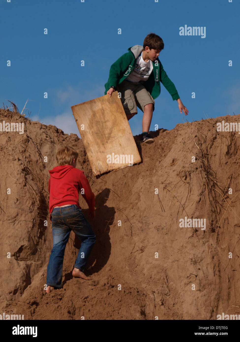 boys using old bit of wood to slide down sand dunes. Exmouth, Devon, UK Stock Photo Alamy