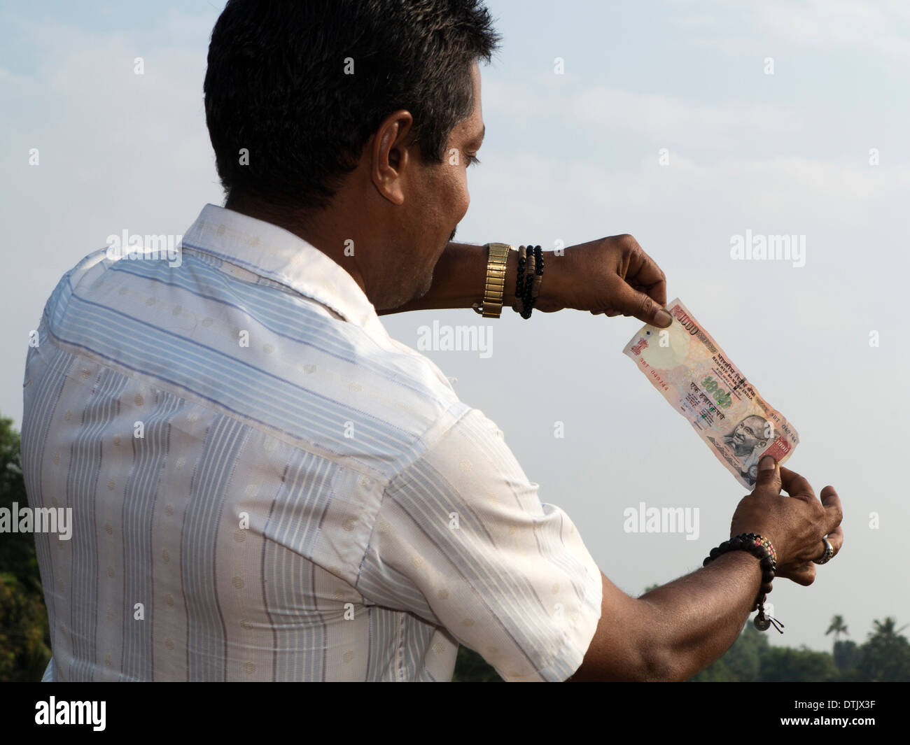 India, Kerala, money, Indian man holding up 1000 rupee note to light to check watermark Stock Photo