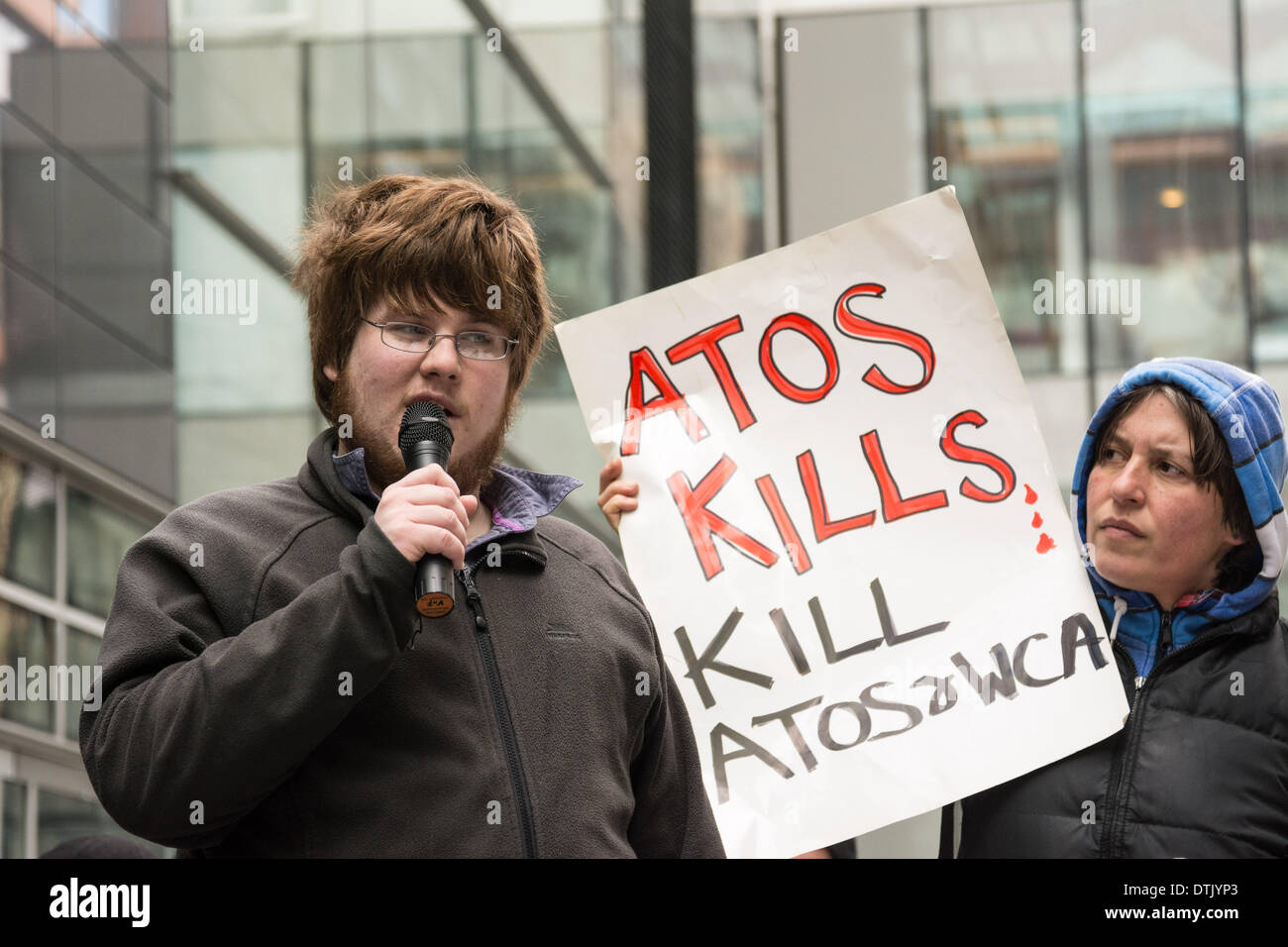 ATOS headquarters, London, UK, 19th February, 2014. A protester speaks as people gather outside ATOS head office in London to protest the company’s implementation of Work Capability Assessments. Protesters say that ATOS workers with little or no medical knowledge make poor decisions which lead to people losing their sickness benefits, and demand that a qualified medical doctor, ideally the GP who regularly sees and treats the sick or disabled person in question, is the only person able to decide if an individual is fit for work. Credit:  Patricia Phillips/Alamy Live News Stock Photo
