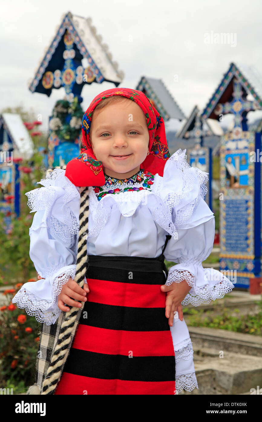 Little girl wearing Romanian traditional clothing and traditional cemetery of Sapanta on a background Stock Photo