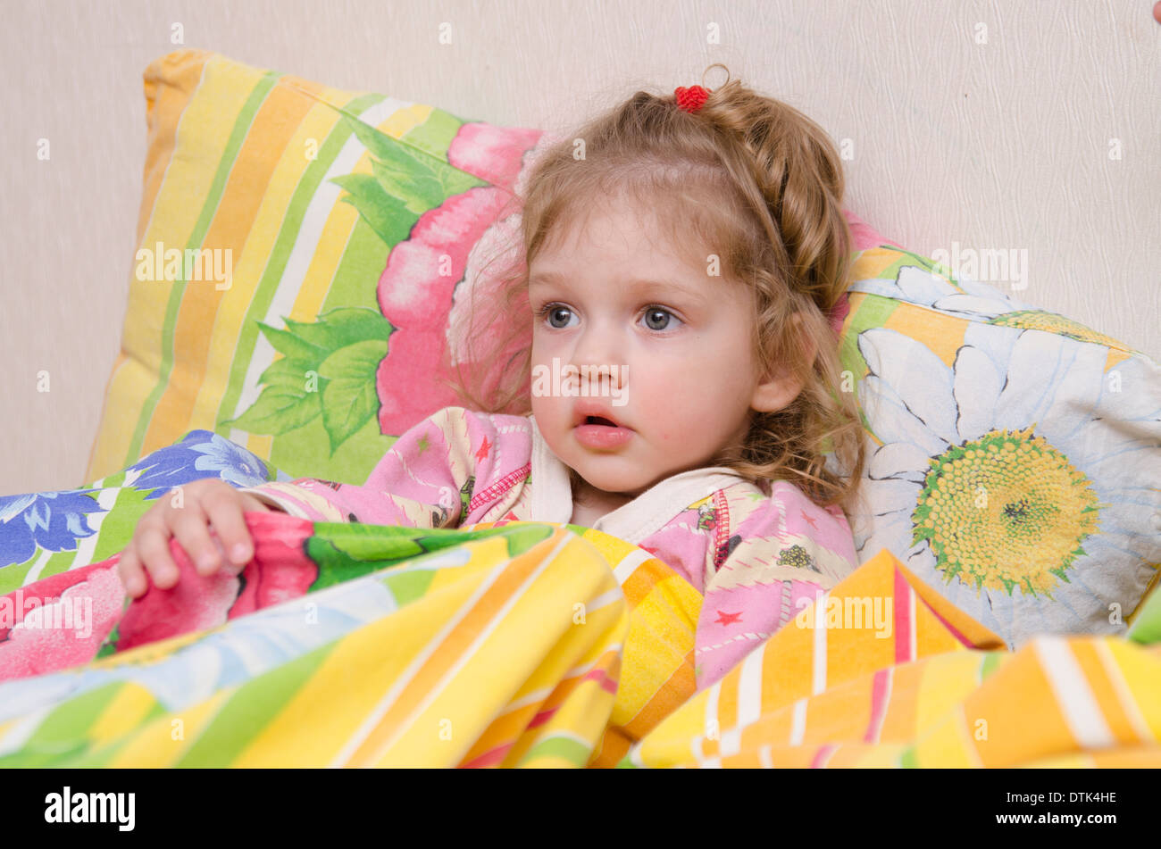 Twoyearold girl is in bed. Pillow put to the wall and covered her bright blanket. Home