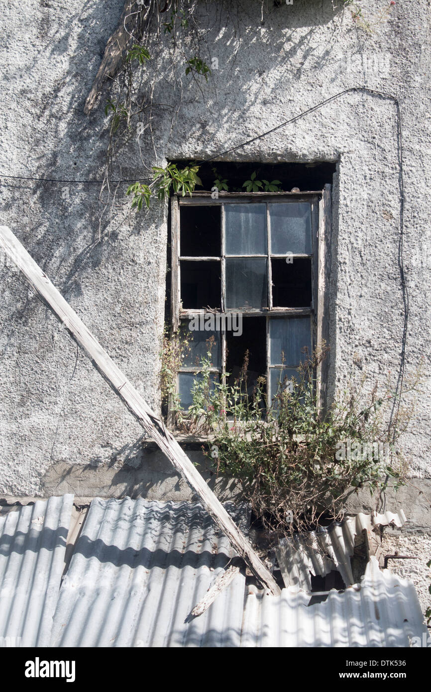 Derelict house broken window with wooden beam fallen through corrugated