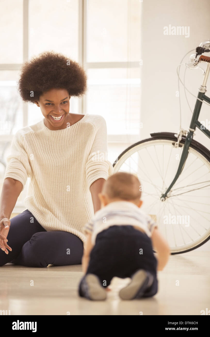 Mother watching baby boy crawl in living room Stock Photo
