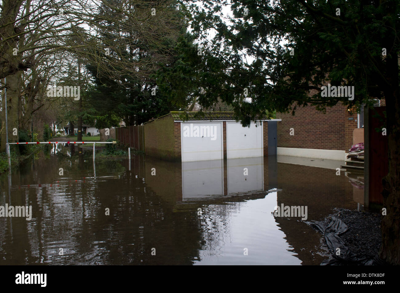 Flooded residential area and park in Staines. Driveway totally flooded with sandbags and wooden board covering front door and steps for protection. Driveway has twin white garages. Stock Photo
