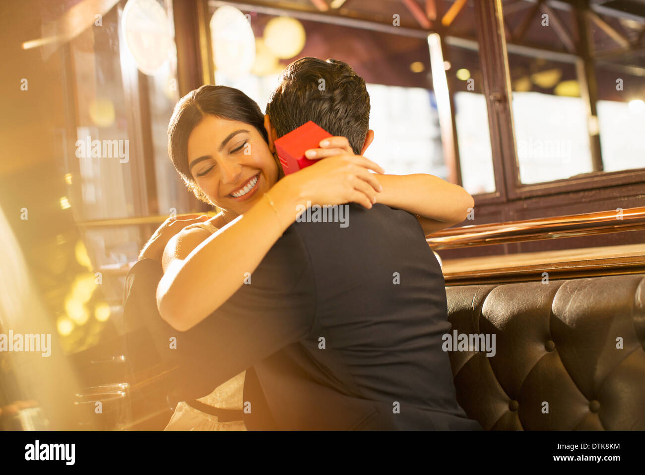 Woman with jewelry box hugging man in restaurant Stock Photo