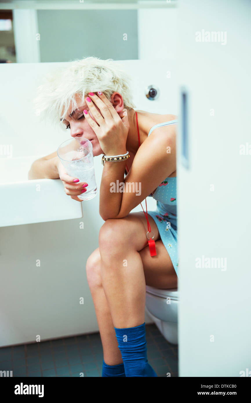 Hungover woman sitting on toilet in bathroom Stock Photo