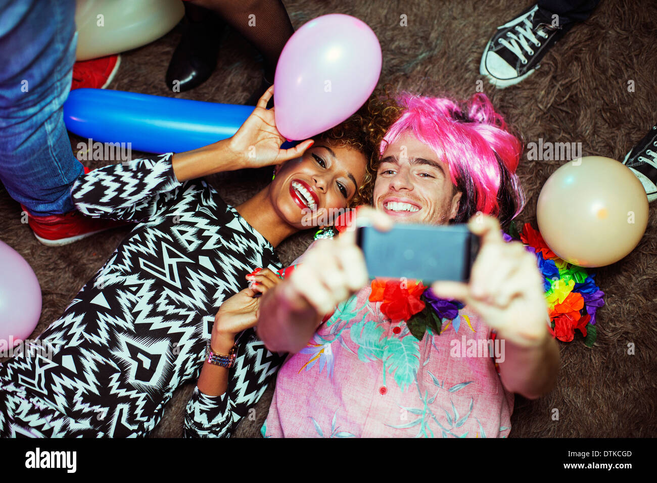 Couple taking self-portrait with cell phone on floor at party Stock Photo