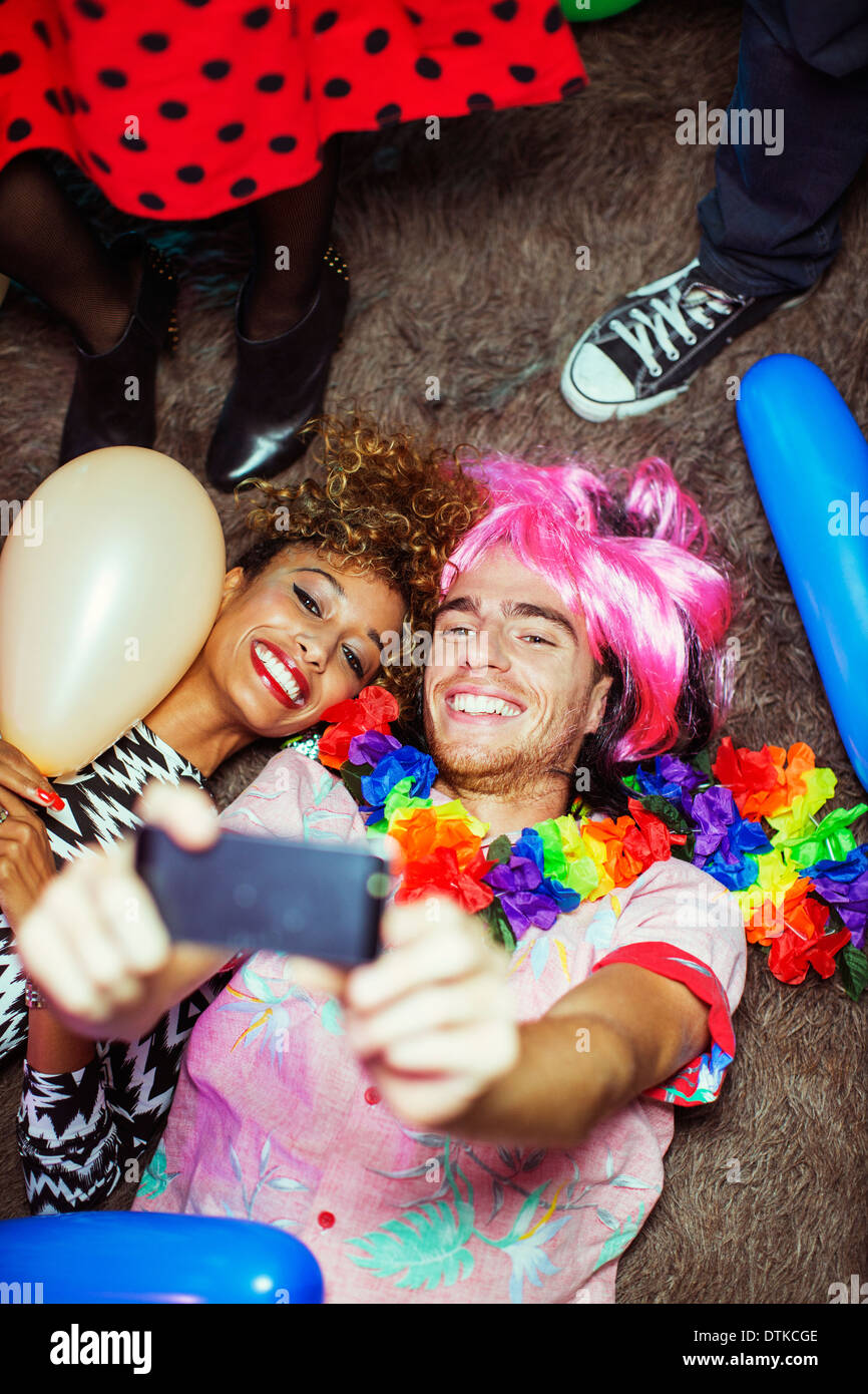 Couple taking self-portraits with camera phone on floor at party Stock Photo