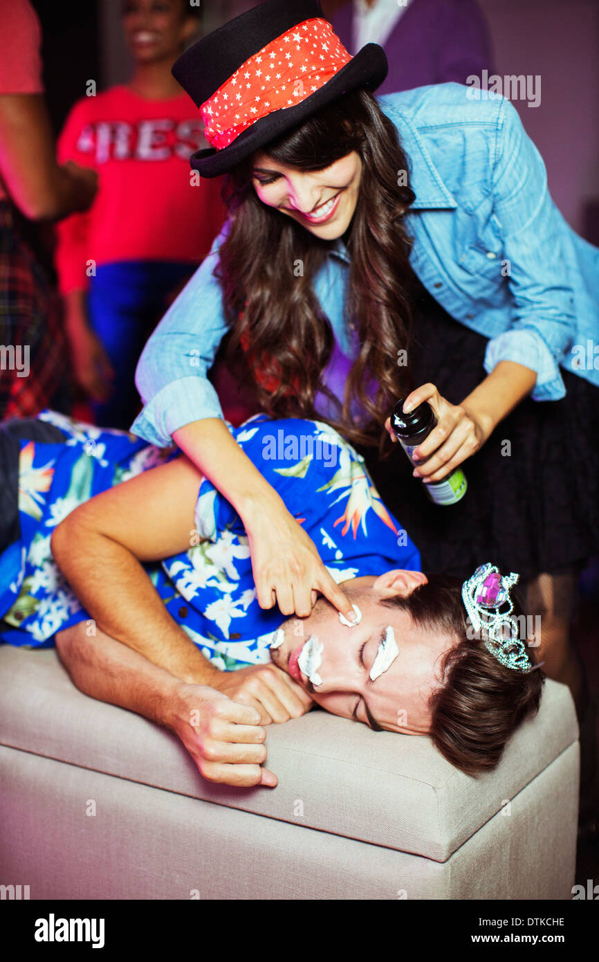 Woman spraying shaving cream on sleeping man's face at party Stock Photo