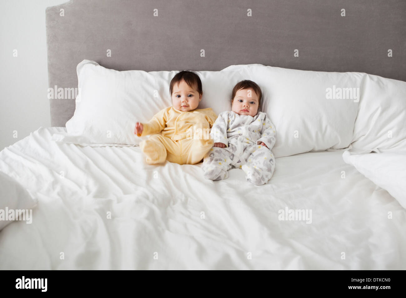 Twin baby girls sitting on bed Stock Photo