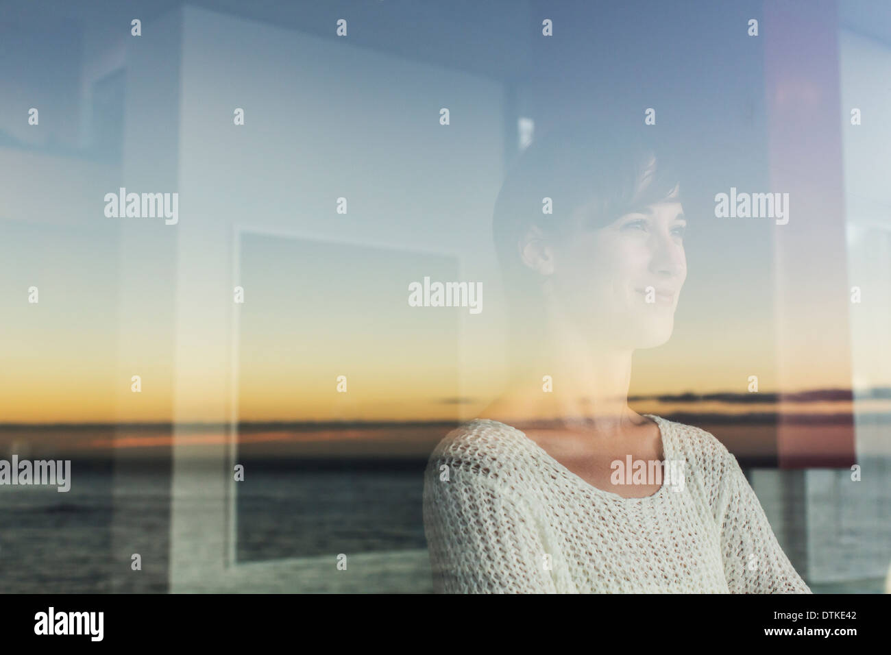 Woman overlooking sunset and ocean from window Stock Photo