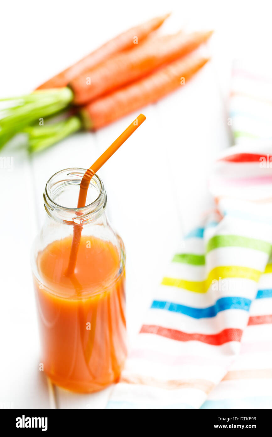 bottle of carrot juice with straw on kitchen table Stock Photo