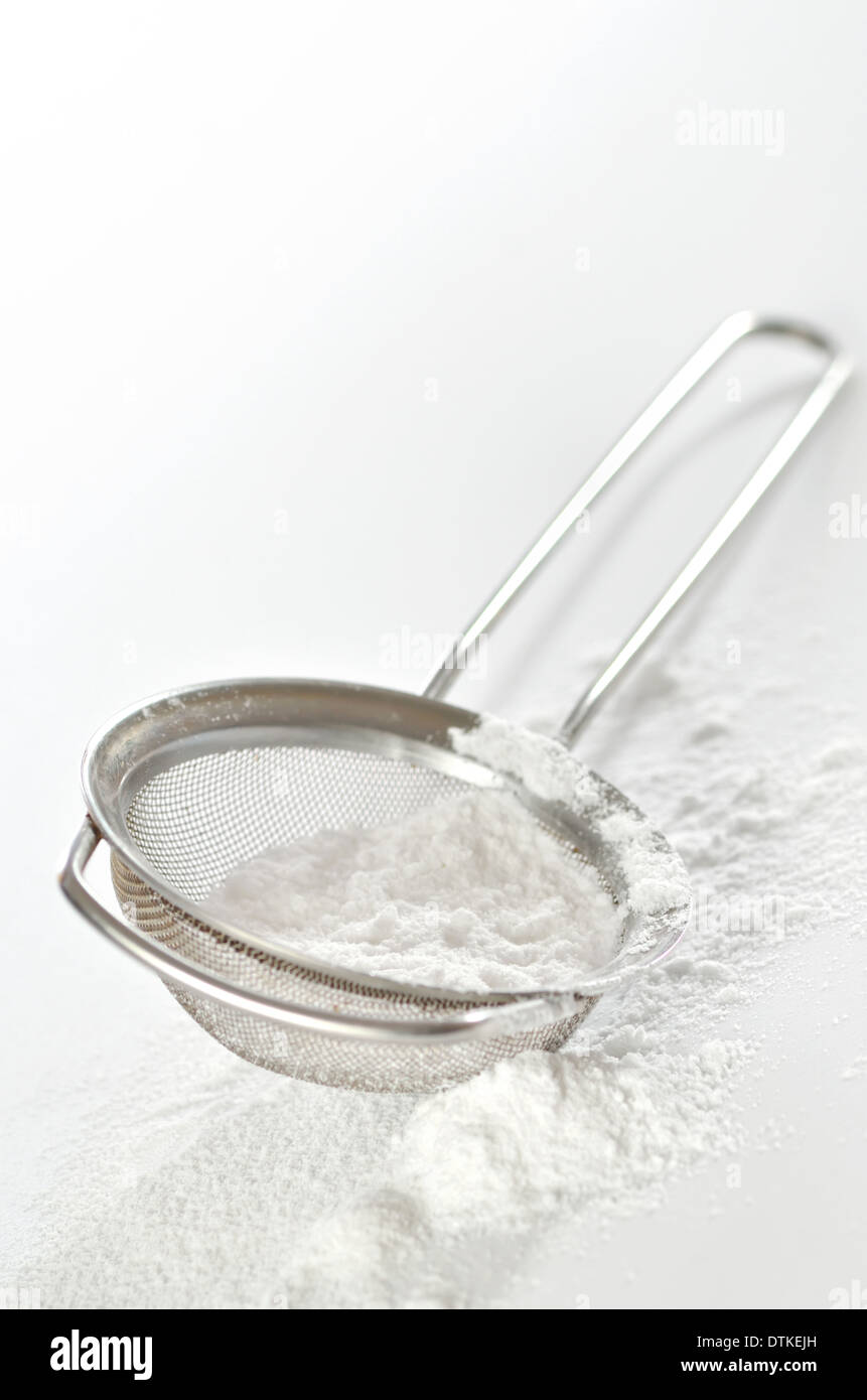 powdered sugar in a metal strainer on white background Stock Photo