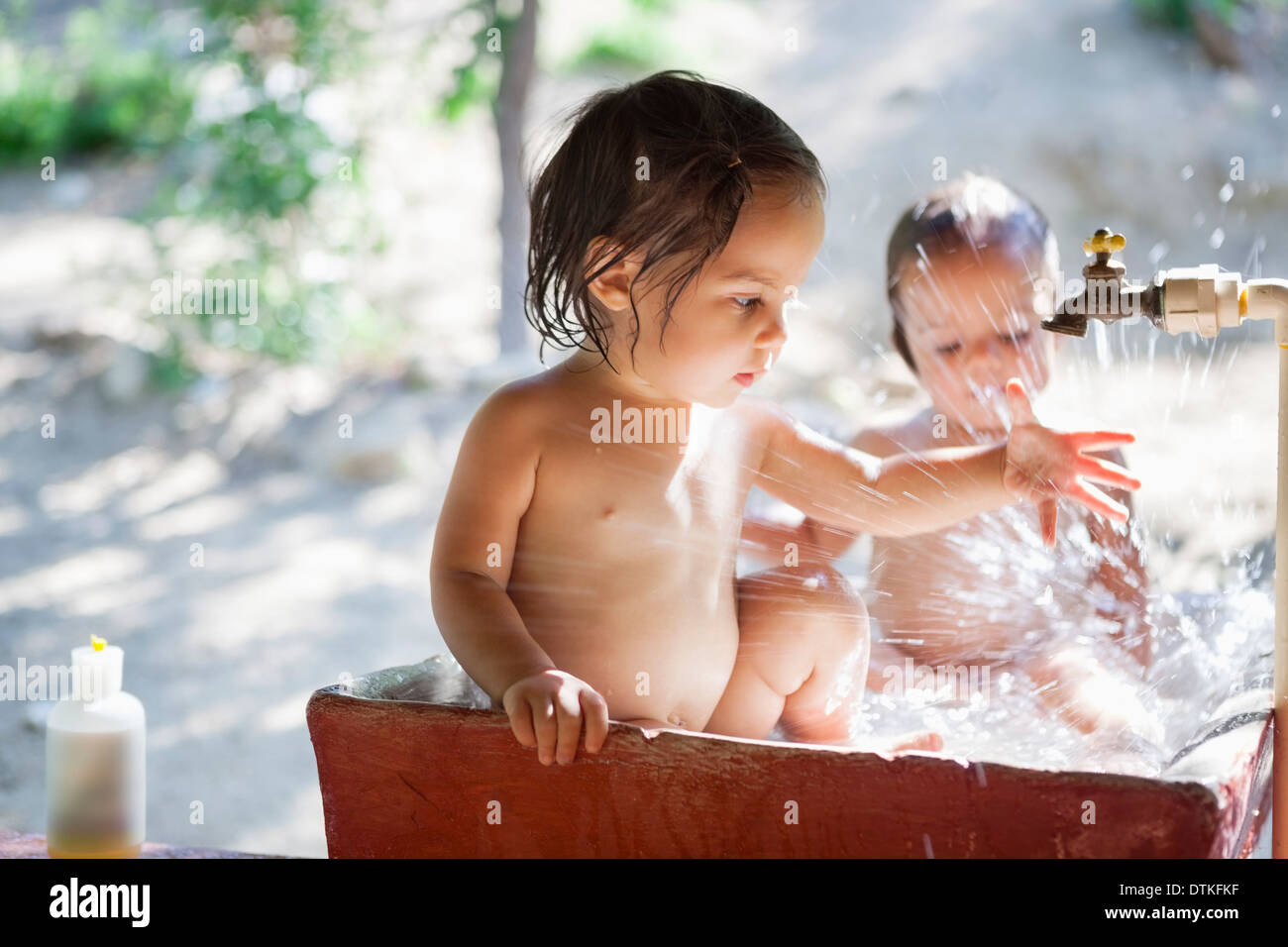 Baby girls playing in water spout outdoors Stock Photo