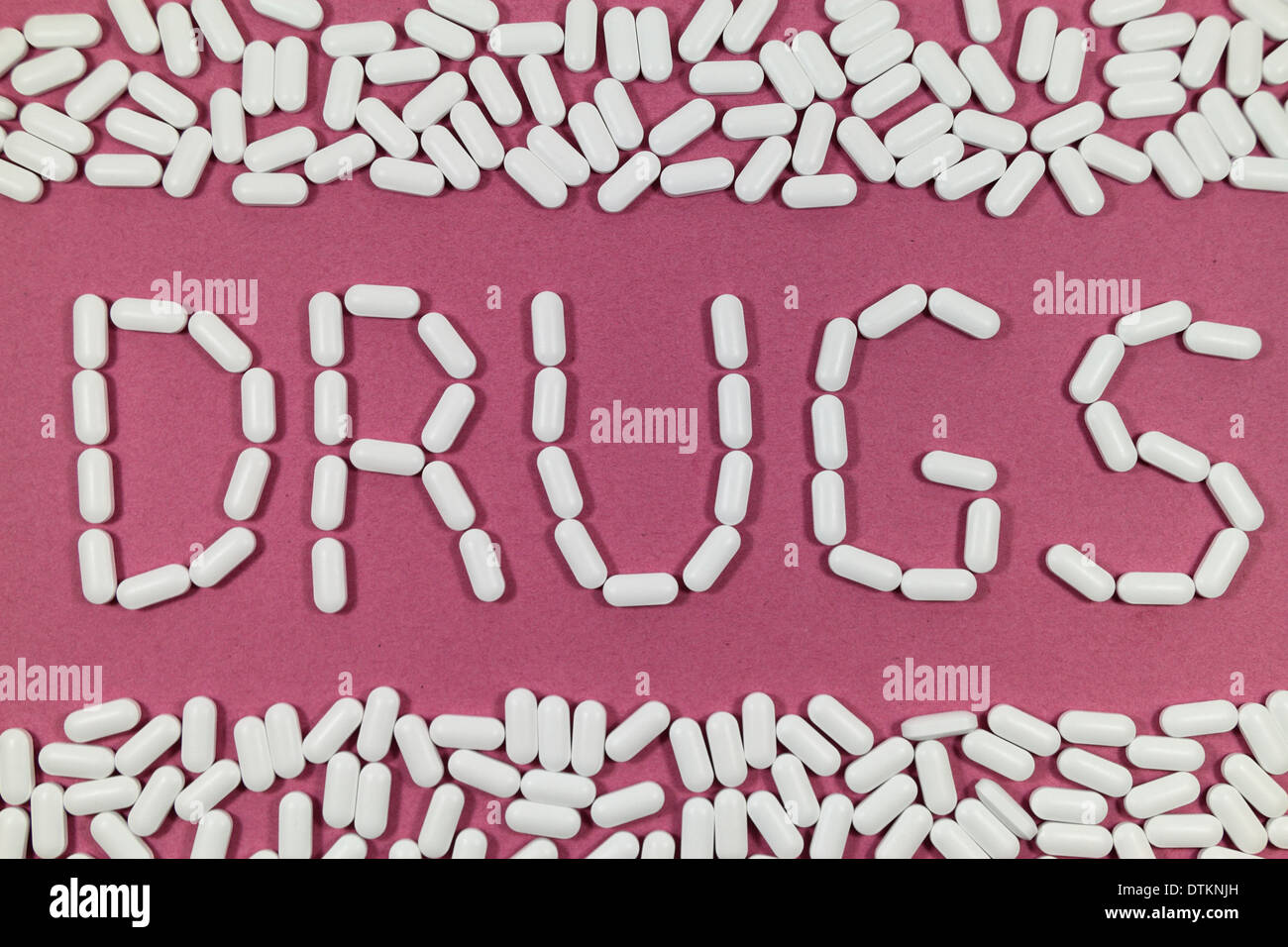 White pills on a red/pinks background spelling 'DRUGS'. Stock Photo