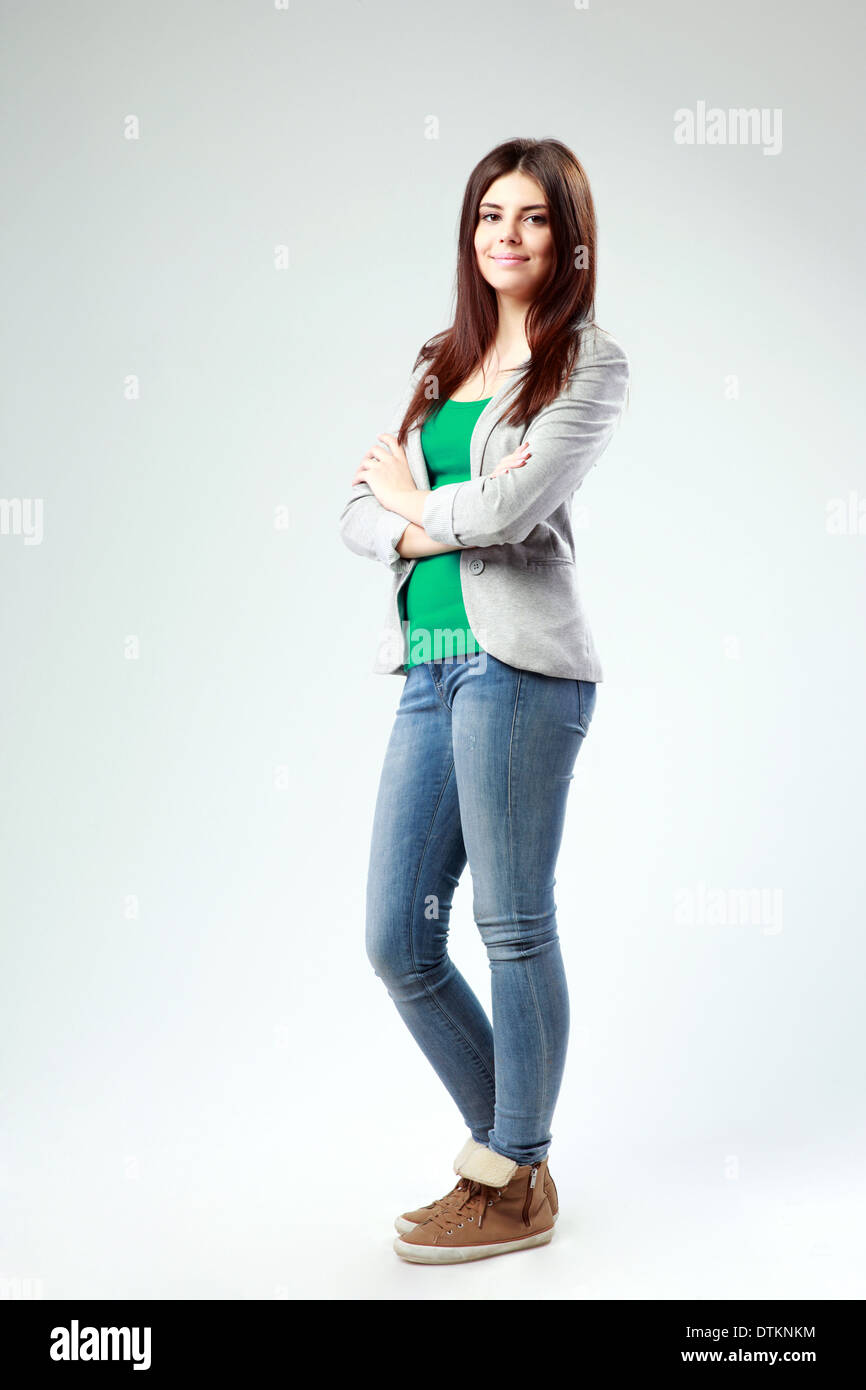 Full-length portrait of a young cheerful woman with arms crossed on gray background Stock Photo