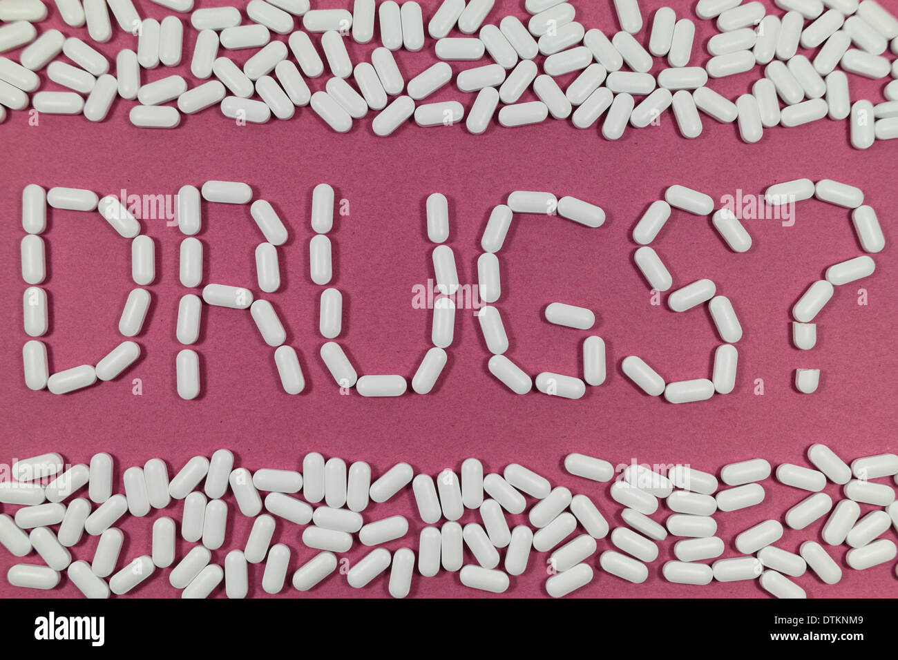 White pills on a red/pink background spelling 'DRUGS?'. Stock Photo