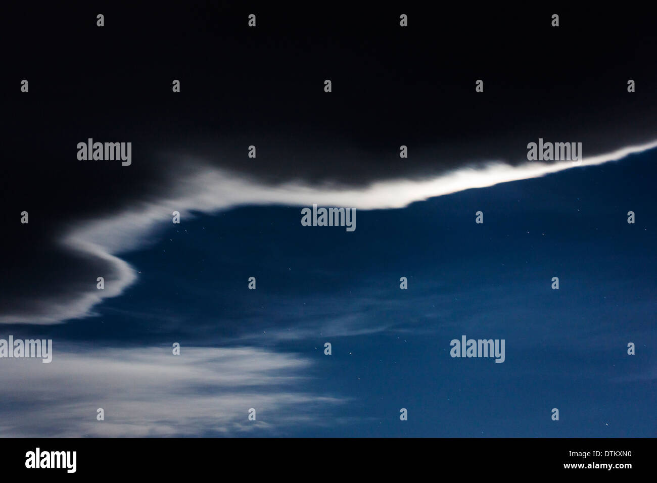 Full moon backlights the edge of an unusual star studded night time cloud formation. Stock Photo