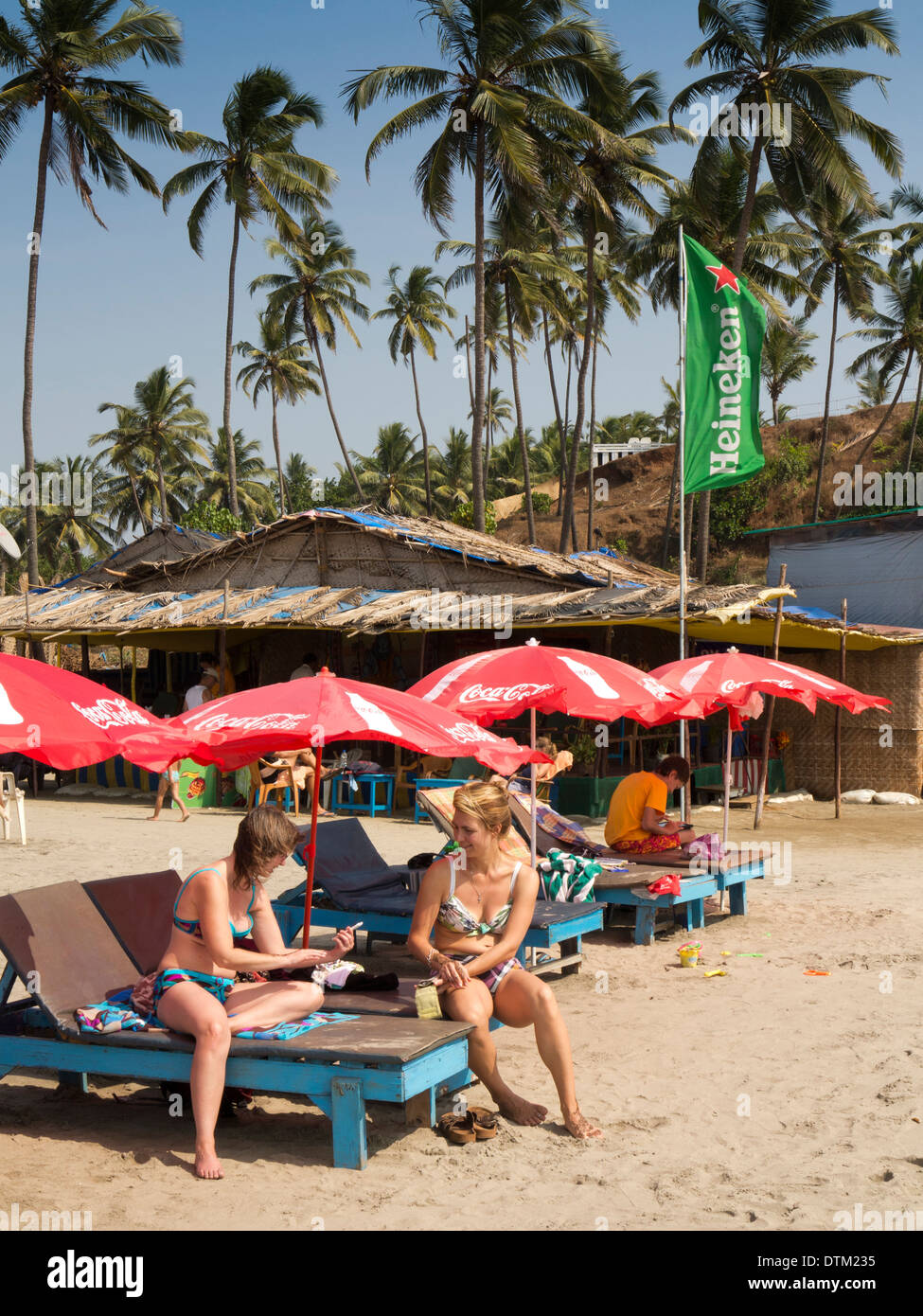 India, Goa, Big Vagator beach, Russian women tourists on sunloungers at bar below tall coconut palm trees Stock Photo