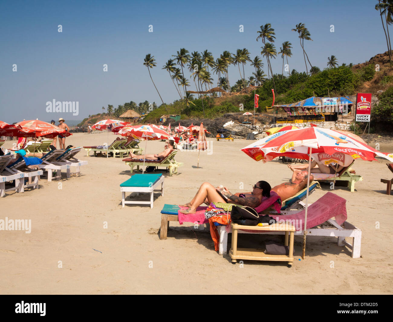 India, Goa, Big Vagator beach, Russian tourists on sunloungers at bars below tall coconut palm trees Stock Photo