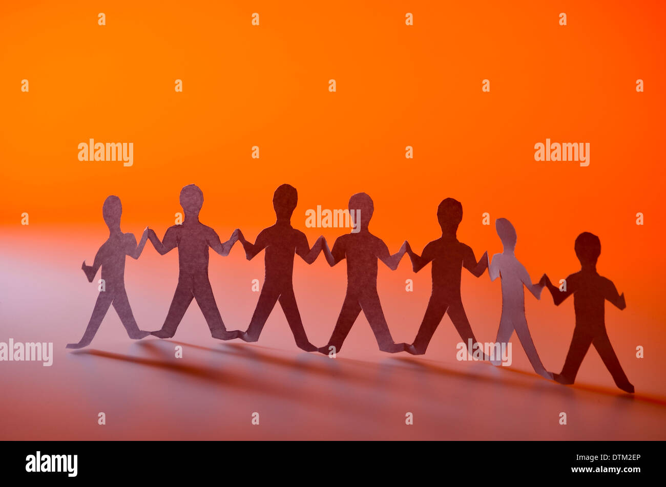 Close up of a paper chain people with shadow and orange background Stock Photo