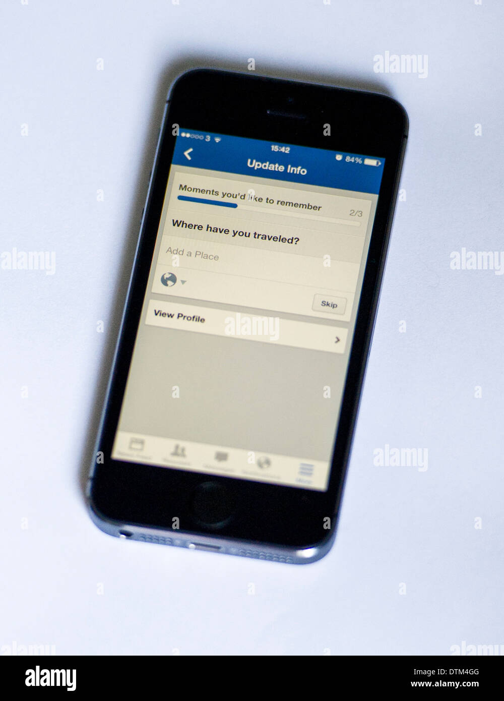 An iPhone 5S on a white  background, showing the Facebook app asking the user where they have traveled. Stock Photo