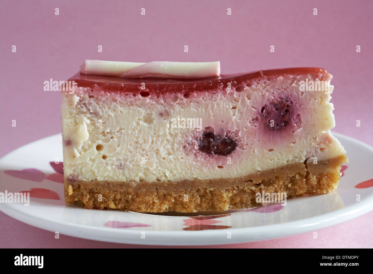Tesco Finest heritage raspberry & swiss white chocolate cheesecake slice on hearts plate set on pink background Stock Photo