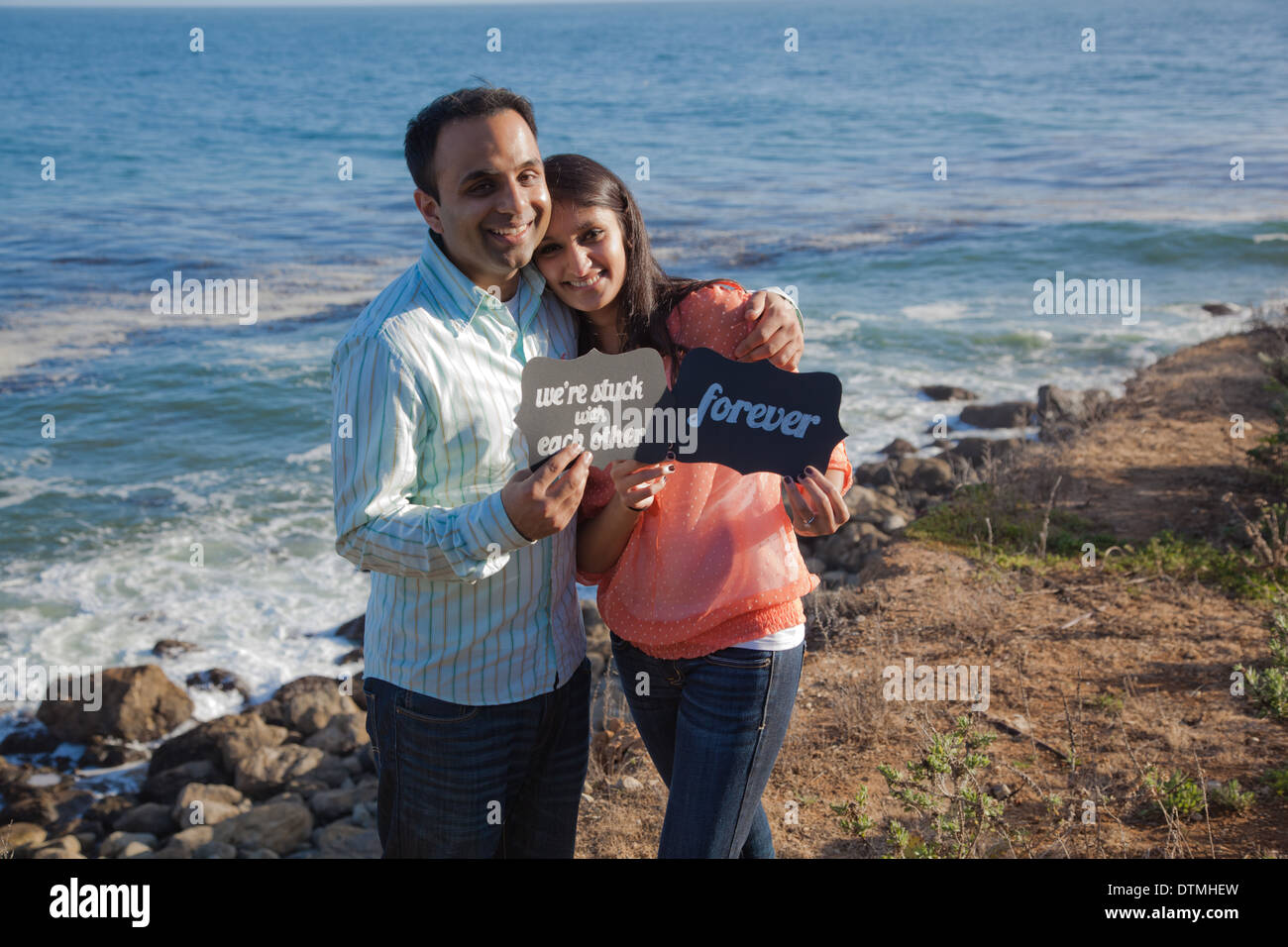 cute indian couple share we're stuck with each other forever signs by the beach ocean sea Stock Photo