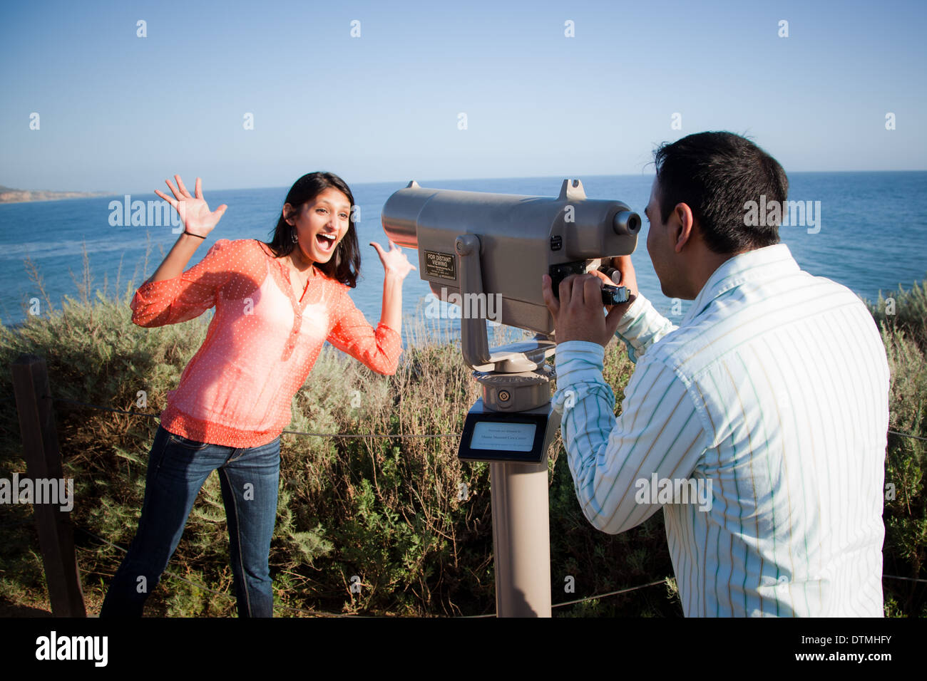 indian couple goof around with a telescope by the beach ocean sea Stock Photo