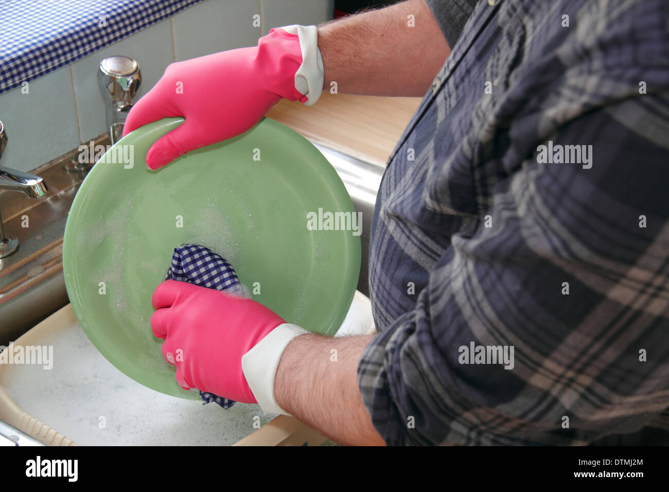 Man washing up pots wearing pink rubber gloves at a kitchen sink at home, England, UK Stock Photo