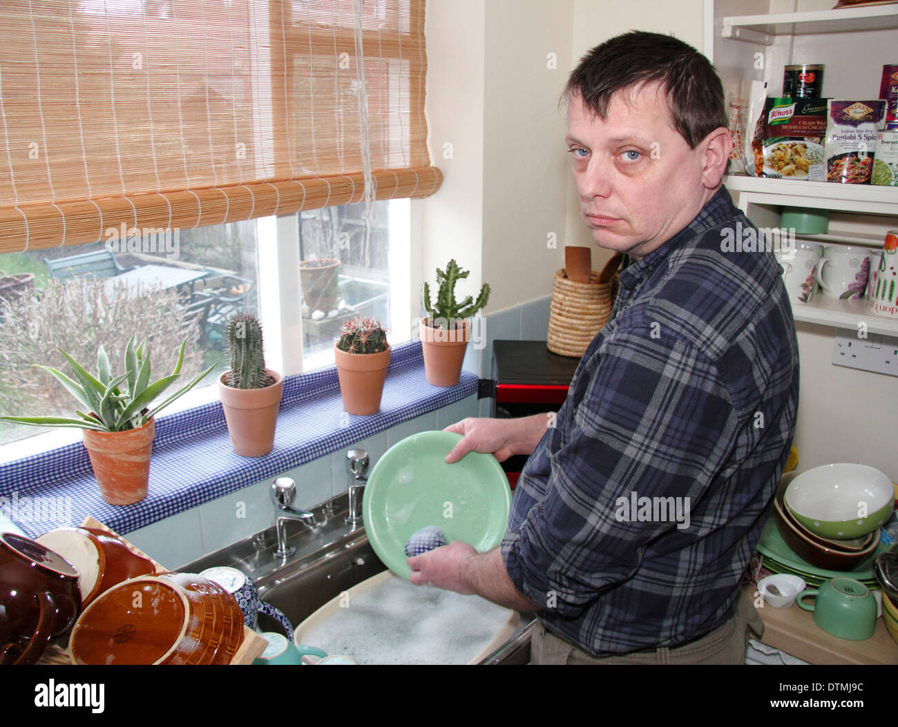 Man washing up pots with little enthusiam  at a kitchen sink at home, England, UK Stock Photo