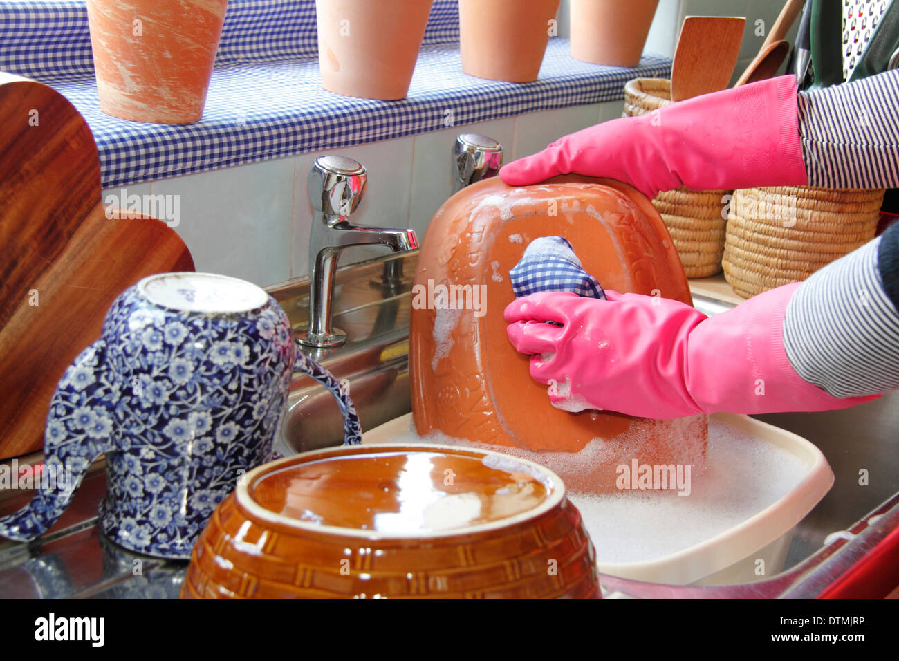 Woman wearing rubber gloves washing up the pots at the kitchen sink at home Stock Photo