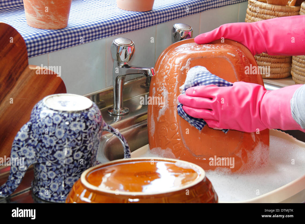 Woman wearing rubber gloves washing up the pots at the kitchen sink at home Stock Photo
