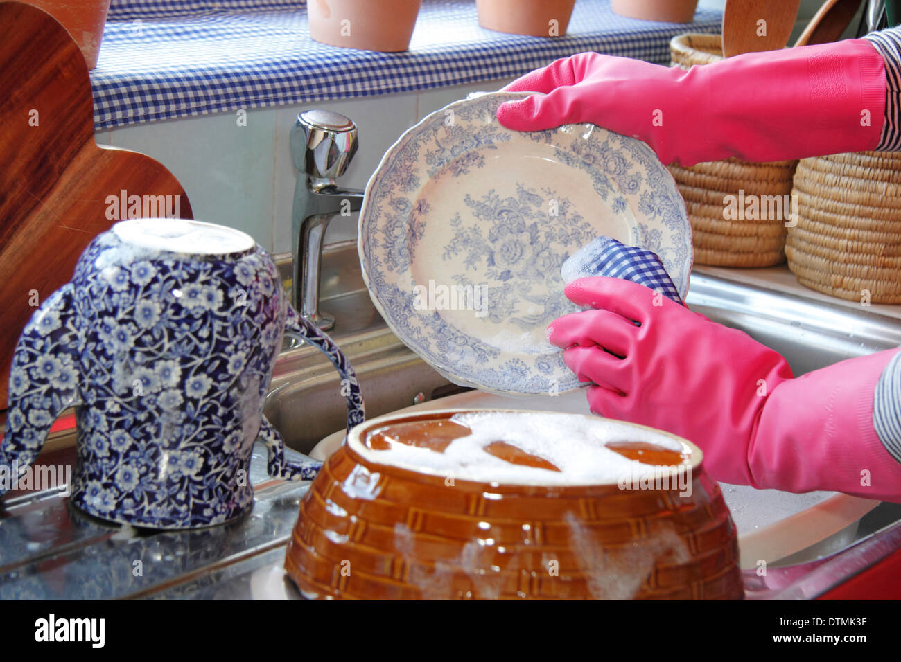 Woman wearing rubber gloves washing up the pots at the kitchen sink at home Stock Photo