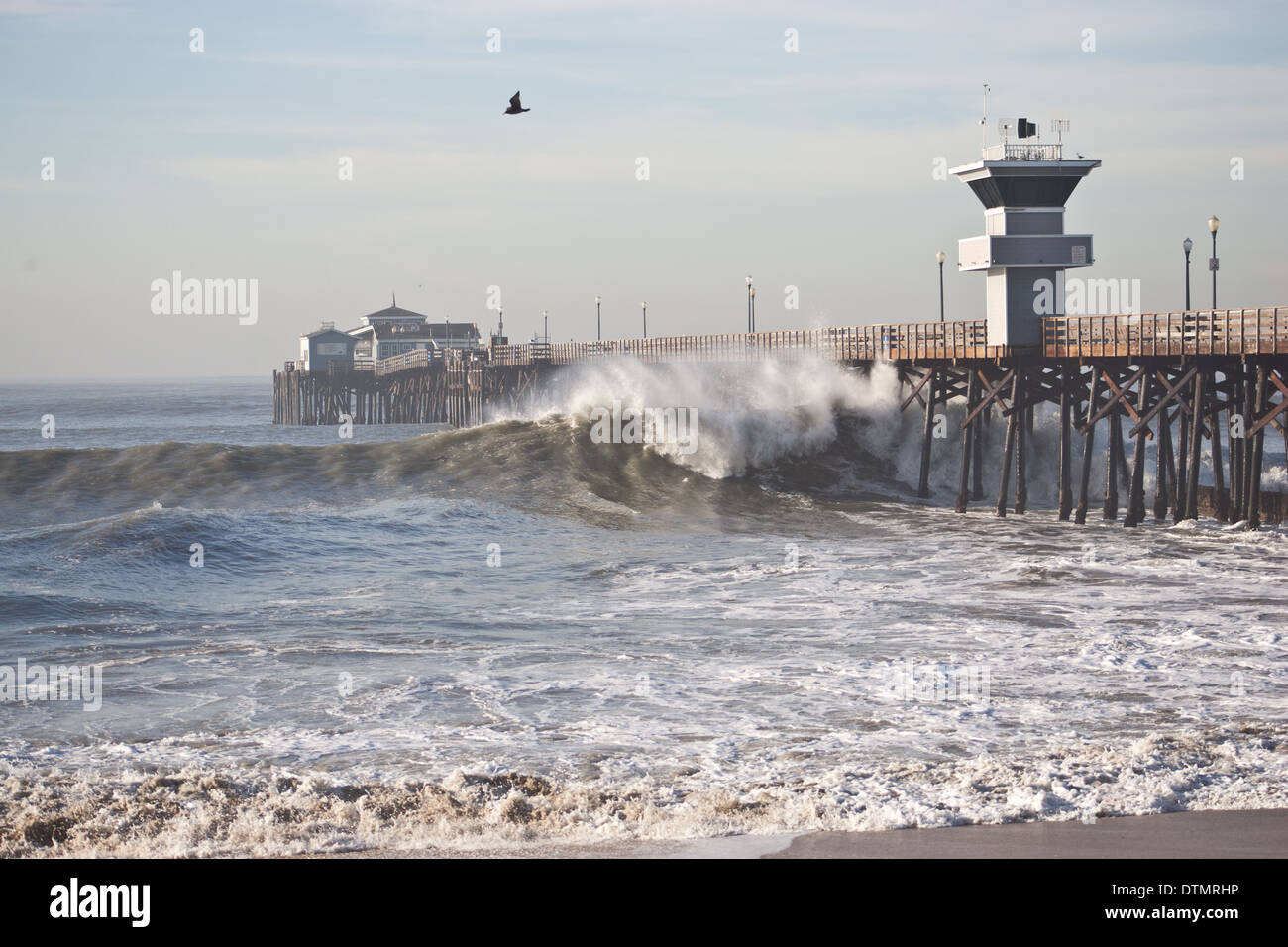 huntington beach california pier with large huge massive waves crashing  against the pier with a bird flying in the sky mid day Stock Photo - Alamy