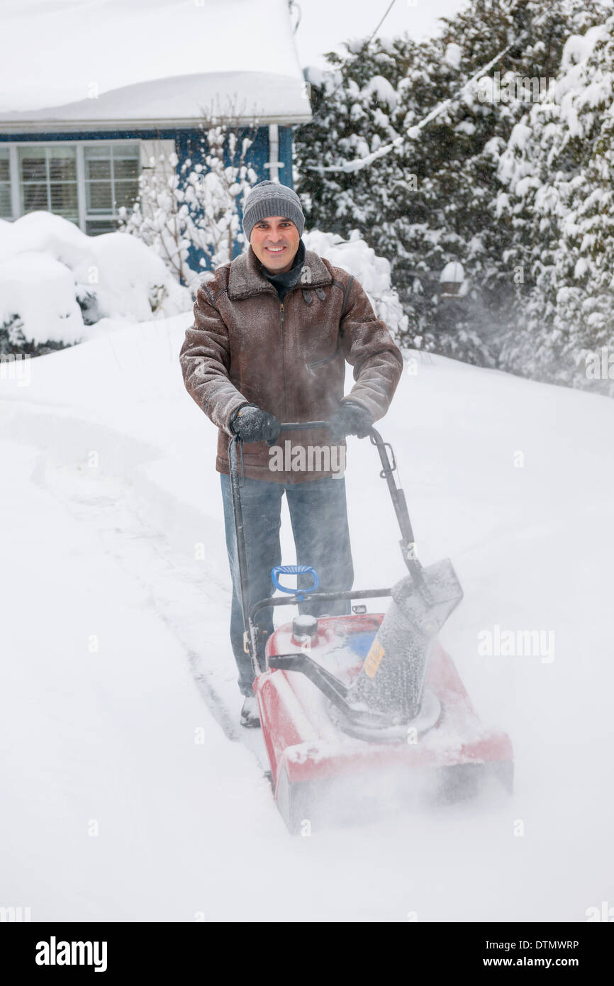 Man using snowblower to clear deep snow on driveway near residential house after heavy snowfall. Stock Photo