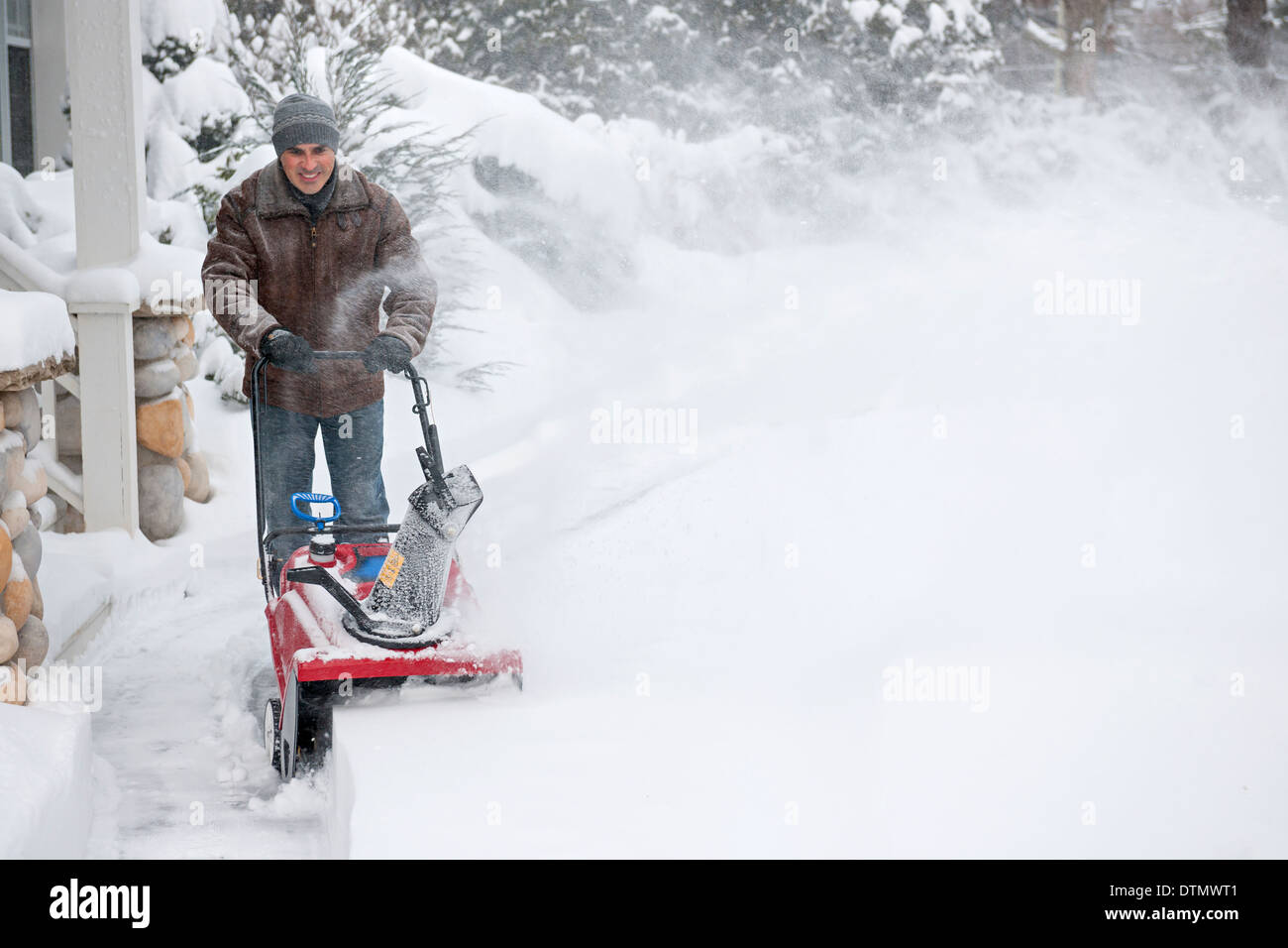 Man using snowblower to clear deep snow on driveway near residential