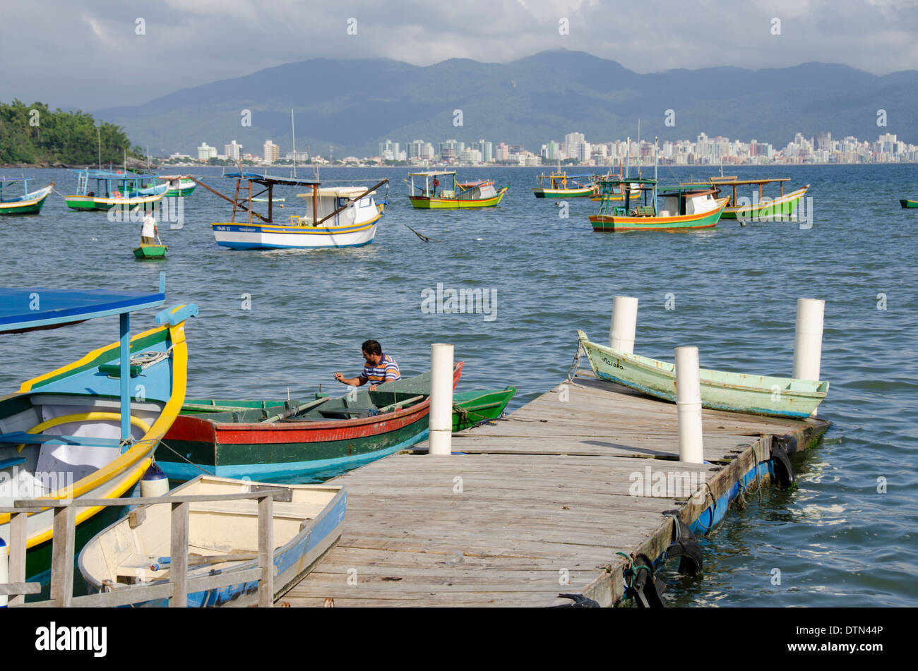 Brazil, Santa Catarina, Porto Belo. Colorful local fishing boats with city skyline in distance. Stock Photo