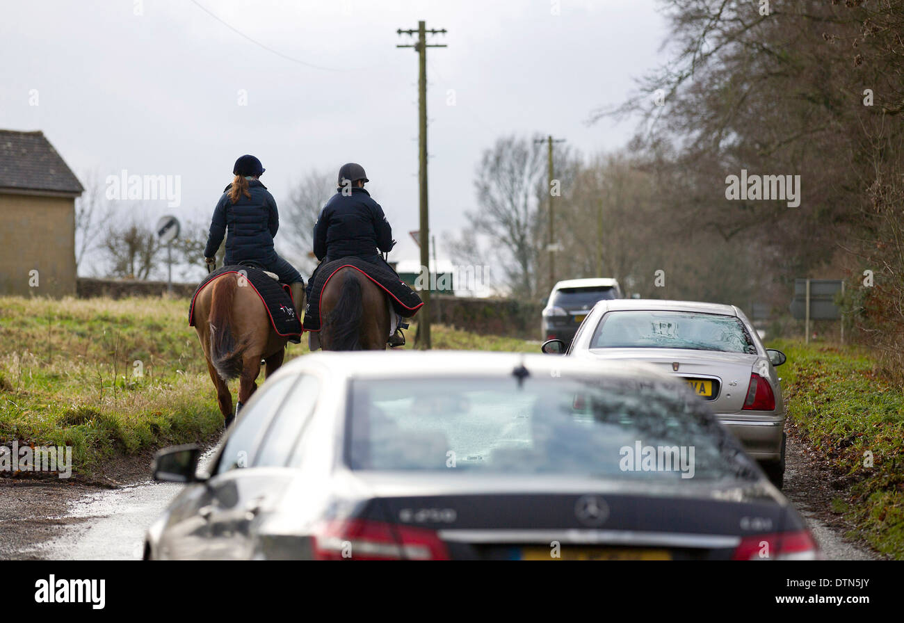 UK, Gloucestershire : Cars travel slowly past horses being ridden along a country road in Gloucestershire. Stock Photo
