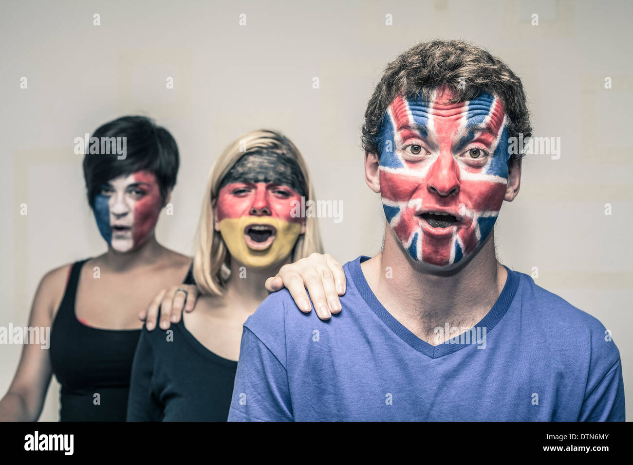 Group of exited people with painted flags on their faces shouting. Stock Photo