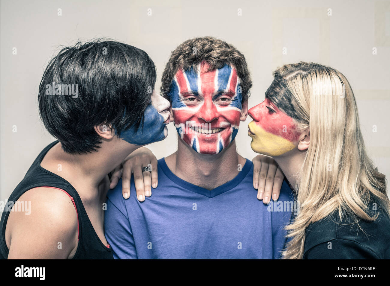 Happy women kissing man with painted European flags on their faces. Stock Photo