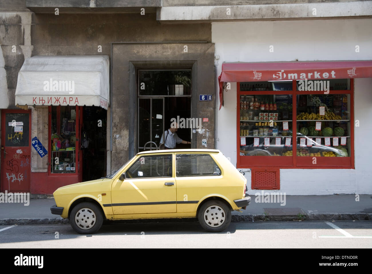 Yellow Zastava parked on street in front of shop fronts in Belgrade Stock Photo