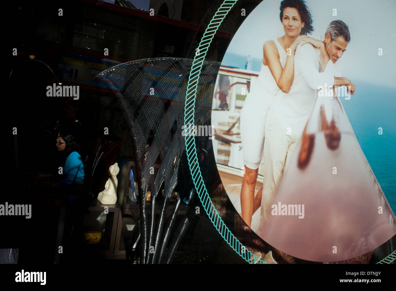 A lady office worker sits at her desk near the romance of a poster for a cruise holiday. Stock Photo